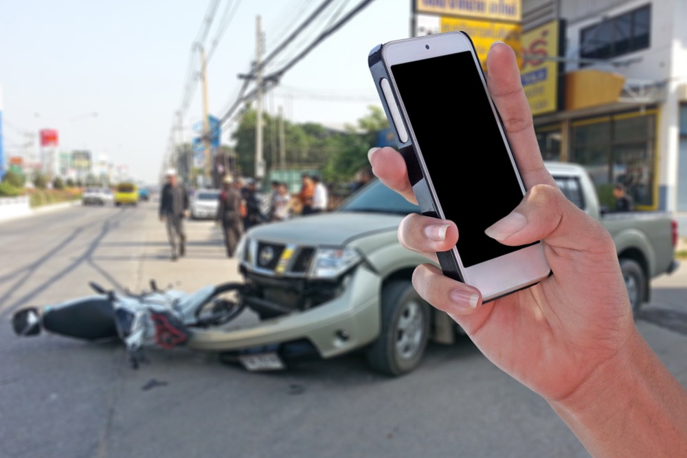 A picture of a person holding a phone and calling a hit and run lawyer with a blurred background of a car accident scene.