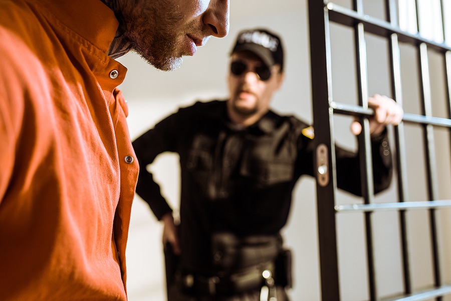 A person in a prison cell with a guard standing outside
