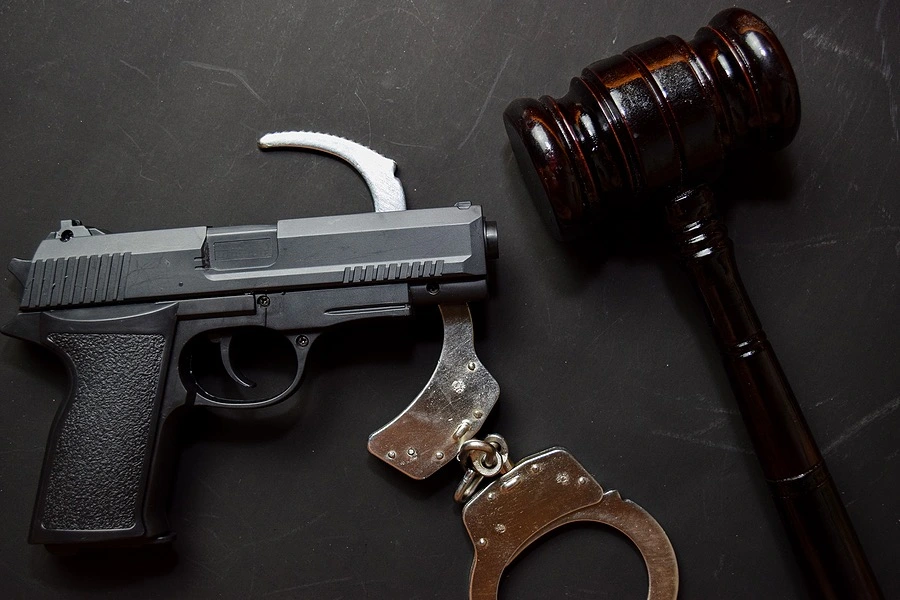 Gun, gavel, and handcuffs lay on a desk, representing the impact on immigration status and gun rights